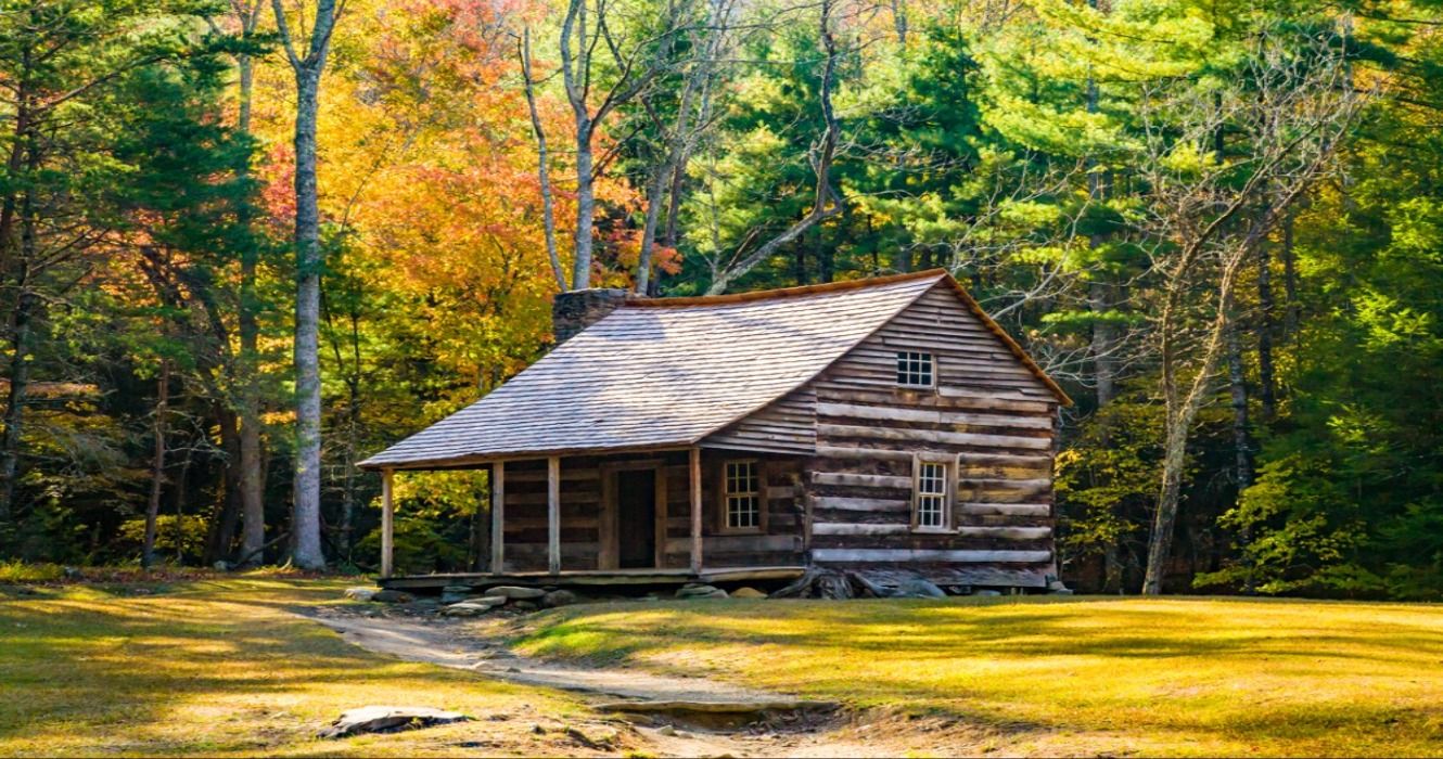 A restored log cabin surrounded by fall foliage in the Cades Cove region of Great Smoky Mountains National Park, Tennessee, USA